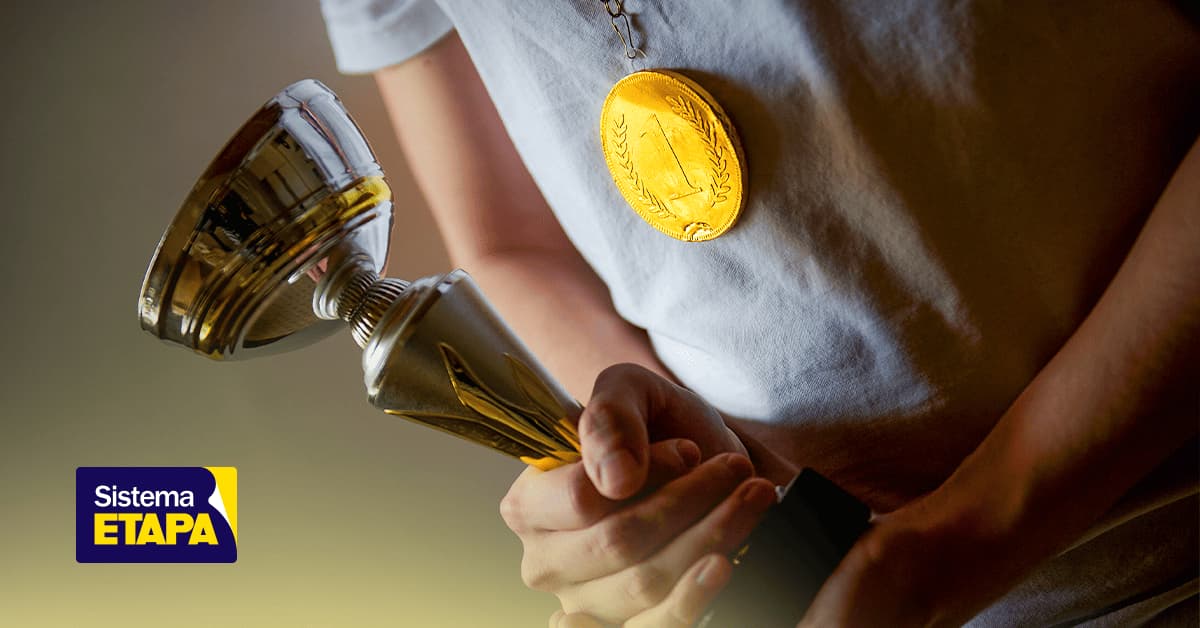 Close-up de uma pessoa segurando um troféu enquanto usa uma medalha dourada.